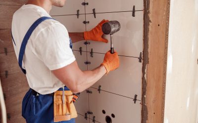 Close up of young man construction worker using rubber hammer while placing tile on the wall